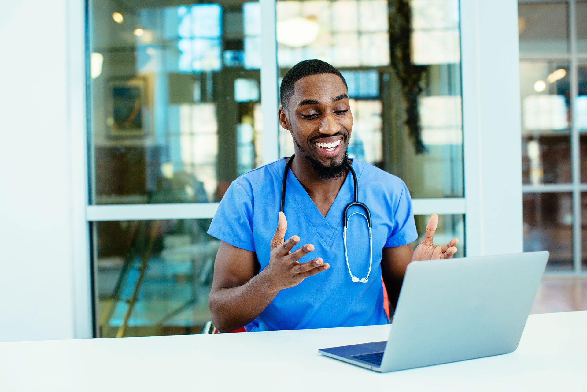 happy male doctor smiling at open laptop and talking with patient during telehealth appointment